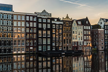 Scenic view of iconic canal houses in Amsterdam with reflections in the water during sunset. HD wallpaper