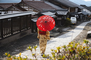 Woman in kimono with red umbrella walking through a traditional Japanese village street. HD wallpaper