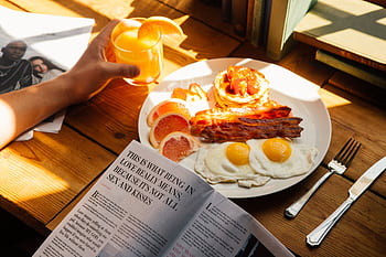 Sunlit breakfast with bacon, eggs, pancakes, and orange juice on a wooden table. HD wallpaper