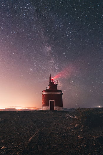 Tranquil scene of a red lighthouse under a starry Milky Way sky at night. HD phone wallpaper