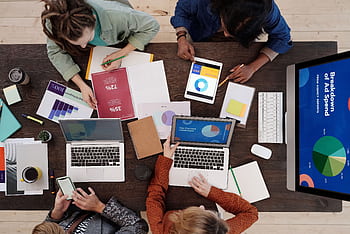 A diverse team collaborating on digital marketing strategies at a desk, using laptops and tablets. HD wallpaper