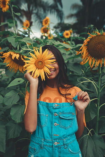 Joyful woman in denim holding sunflower among vibrant blooms in summer garden. HD phone wallpaper