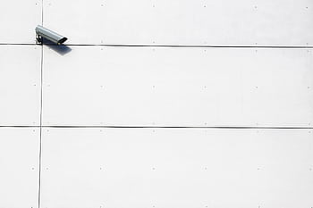 A minimalist showcasing a single surveillance camera mounted on a stark white wall. HD wallpaper