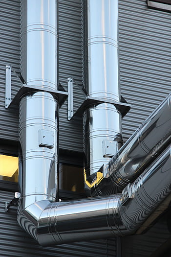 Close-up of shiny stainless steel pipes on an industrial building facade, showcasing modern technology. HD phone wallpaper