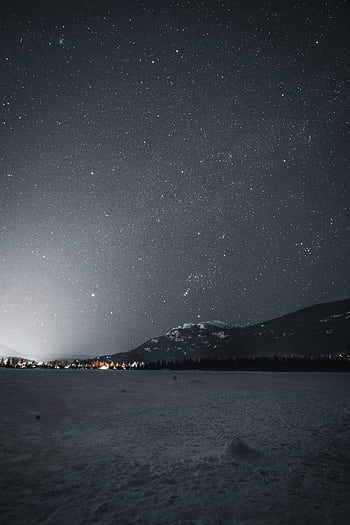 A breathtaking view of a starry night sky over a snowy mountain landscape during winter. HD phone wallpaper