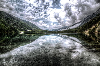 A tranquil mountain lake reflecting clouds and pine forests, creating a breathtaking scenic view. HD wallpaper