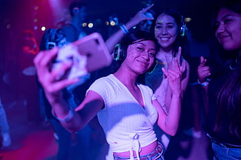 Young adults enjoying a silent disco party, capturing selfies amidst colorful lights. HD wallpaper