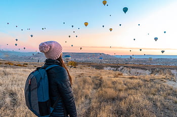 Woman watching hot air balloons in Cappadocia at sunrise, a popular travel destination. HD wallpaper