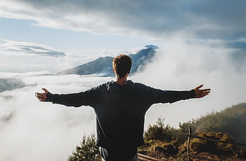 Man with arms outstretched on a misty mountain, embracing nature and tranquility. HD wallpaper