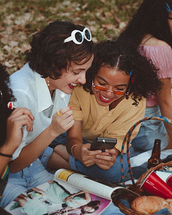 A group of happy young women enjoying a sunny picnic outdoors, engaging with a smart and laughing. HD phone wallpaper
