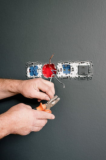 Close-up of an electrician working on electrical outlets, using pliers to repair wiring. HD phone wallpaper