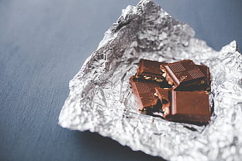 Close-up of a chocolate bar with nuts, partially unwrapped in foil, on a gray surface. HD wallpaper