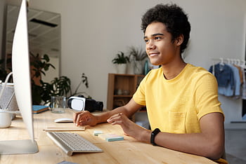 Teenager smiling while studying online at home. Modern education setup with computer and VR headset. HD wallpaper