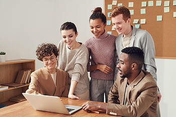Group of diverse professionals engaged in brainstorming session around a laptop indoors. HD wallpaper