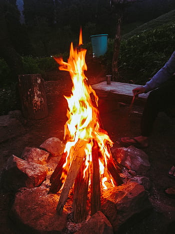 A warm, inviting campfire surrounded by rocks in a peaceful outdoor setting. HD phone wallpaper