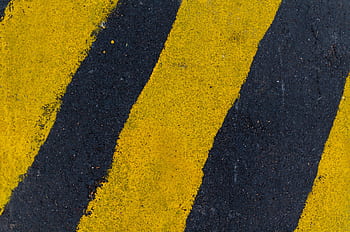 A high-angle close-up of yellow and black road markings on asphalt surface. HD wallpaper