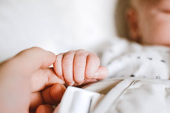 Close-up of a newborn's hand gently gripping a parent's finger, symbolizing love and connection. HD wallpaper