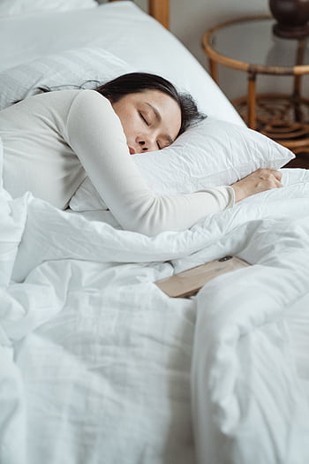 Woman in a cozy bedroom sleeping peacefully, surrounded by white bedding for ultimate comfort. HD phone wallpaper
