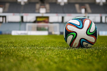 Vibrant soccer ball on a lush green field in an empty stadium. HD wallpaper