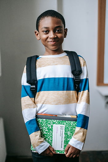 Cheerful schoolboy holding books and smiling in a classroom setting, ready for learning. HD phone wallpaper