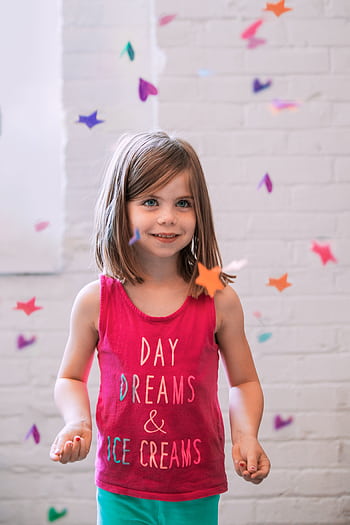 Cheerful child in a colorful shirt surrounded by falling confetti indoors. HD phone wallpaper