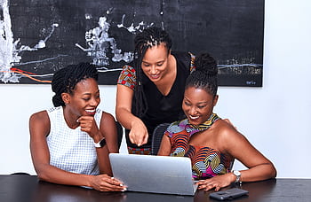 Three African American women collaborating at a laptop, focused and happy during a meeting indoors. HD wallpaper