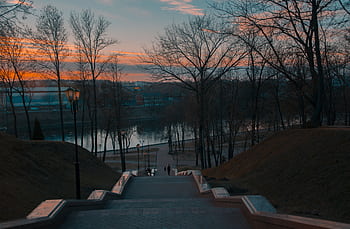 Captivating sunset view over riverbanks in Vitebsk, Belarus, with silhouettes of trees and a serene pathway. HD wallpaper