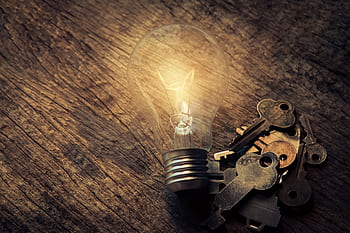 Illuminated vintage light bulb beside keys on rustic wooden table, symbolic of ideas. HD wallpaper