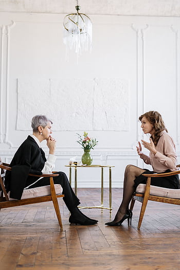 Two women engaged in a counseling session in a bright, modern loft setting. HD phone wallpaper