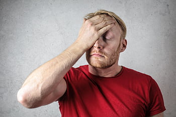 A frustrated man in a red shirt holds his head in stress against a neutral background. HD wallpaper