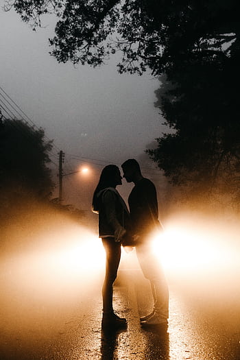 Silhouetted couple standing in front of car headlights on a foggy night, embracing romance. HD phone wallpaper