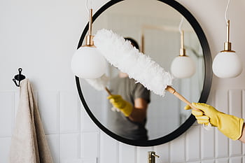 A person cleaning an elegant bathroom mirror with a fluffy duster and yellow gloves. HD wallpaper