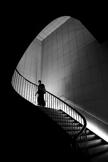 A silhouette of a person ascending a modern, curved staircase in black and white. HD phone wallpaper