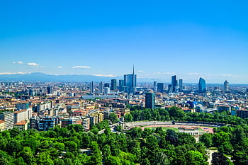 Panoramic view of Milan's skyline featuring modern skyscrapers and lush greenery under a clear blue sky. HD wallpaper