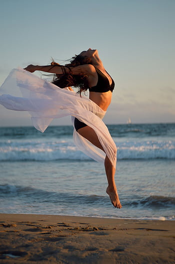 A care woman joyfully dances on the beach at sunset, showcasing dom and elegance with the ocean backdrop. HD phone wallpaper