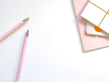 A minimalist flat lay of pink pens and pastel notebooks on a smooth white background, ideal for office and school themes. HD wallpaper