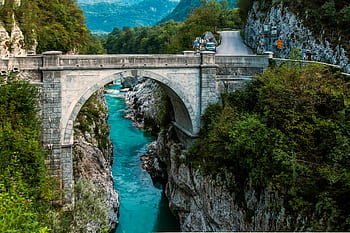Scenic view of a stone arch bridge over a vibrant turquoise river framed by lush greenery. HD wallpaper