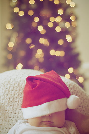 Cute baby wearing a Santa hat with blurred Christmas lights in background. HD phone wallpaper