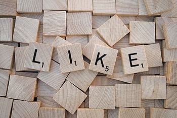 Top-down view of Scrabble tiles spelling 'LIKE' on a pile of blank wooden tiles. HD wallpaper