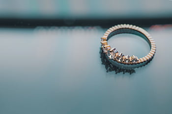 Close-up of a gold ring with diamonds on a reflective surface, showcasing elegance and luxury. HD wallpaper