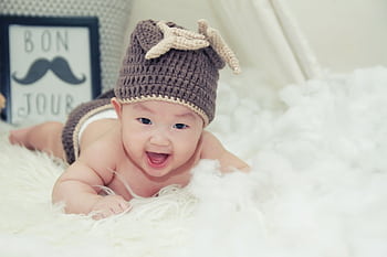 A joyful baby wearing a brown knitted hat lies on a soft surface, radiating happiness. HD wallpaper