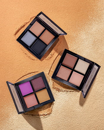 Colorful eyeshadow palettes on a sand-textured backdrop, perfect for beauty and makeup themes. HD phone wallpaper