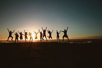 Silhouette of a group of friends jumping on a beach at sunset, expressing joy and dom. HD wallpaper