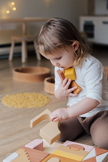 Young child playing with wooden blocks indoors, showcasing innocence and creativity. HD phone wallpaper