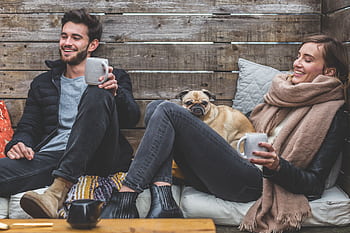Two friends enjoying a warm drink outdoors with their pug on a cozy day. HD wallpaper