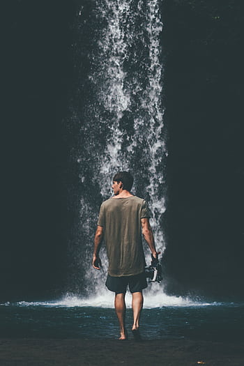 A man stands by a stunning waterfall in Bali, capturing the scenic beauty. HD phone wallpaper