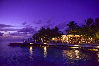 A breathtaking view of a tropical resort at twilight, surrounded by palm trees and reflecting on the ocean. HD wallpaper