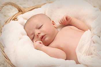 A peaceful sleeping baby nestled in a soft, fluffy blanket inside a wicker basket. HD wallpaper