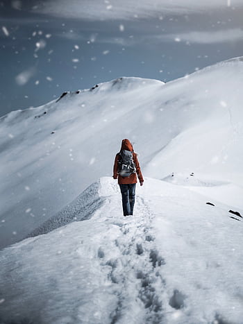 A lone hiker in a red jacket walks up a snow-covered mountain path during a snowfall. HD phone wallpaper