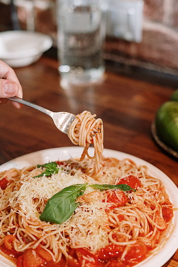 Close-up of a hand twirling spaghetti with tomato sauce and basil, perfect Italian meal. HD phone wallpaper
